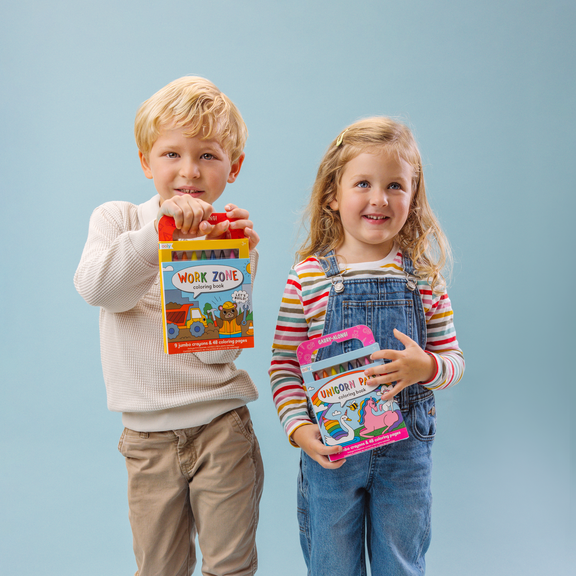 Two kids holding a Work Zone and Unicorn Pals set of Carry Along! Coloring Book and Crayon set