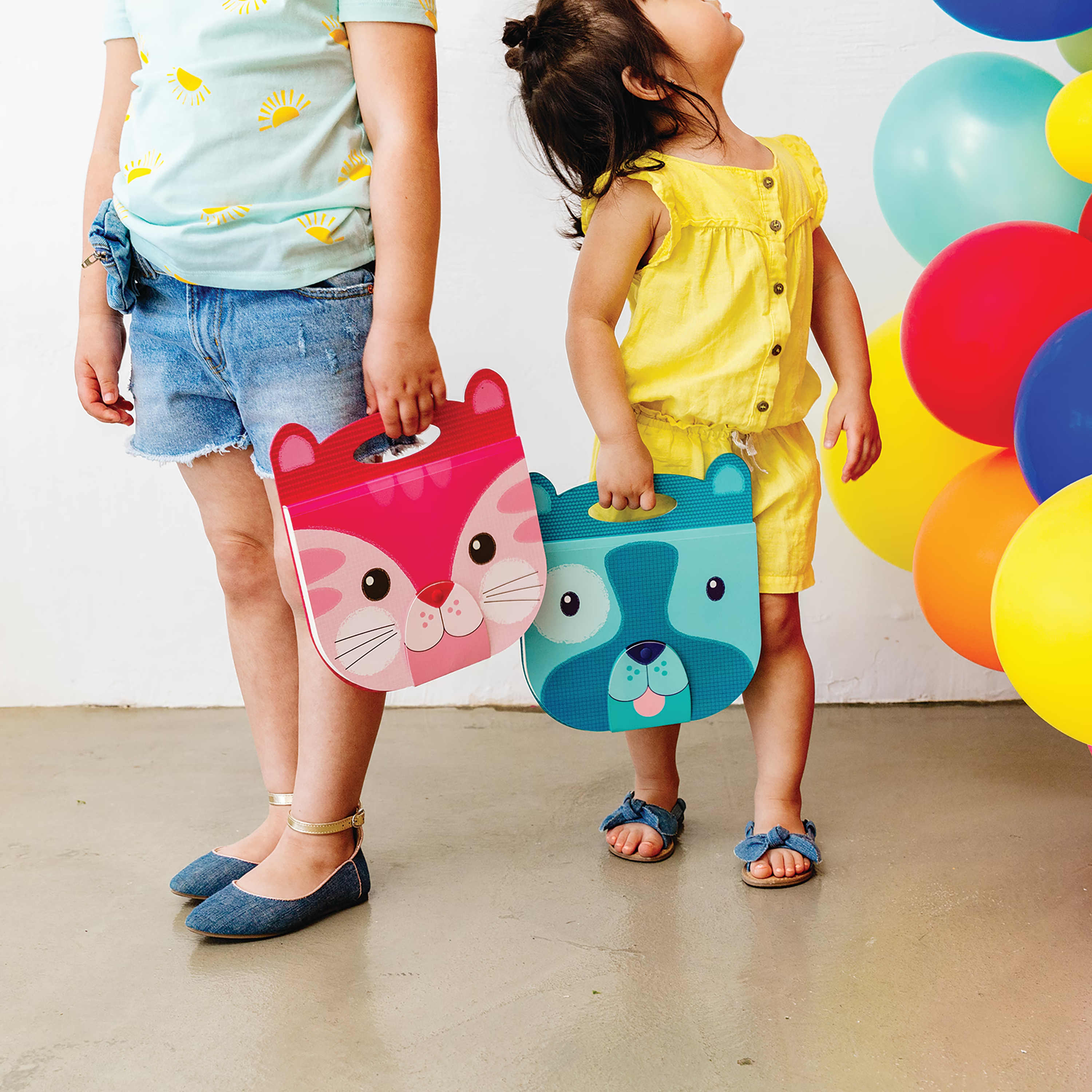 Two people holding OOLY Carry Along Sketchbooks with colorful balloons in background