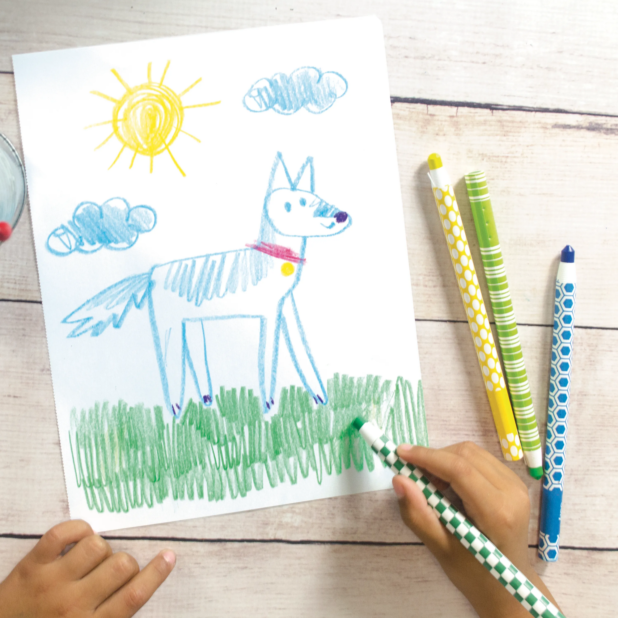 Kid coloring picture of a dog with sun, grass and clouds with OOLY Color Appeel Crayon Sticks