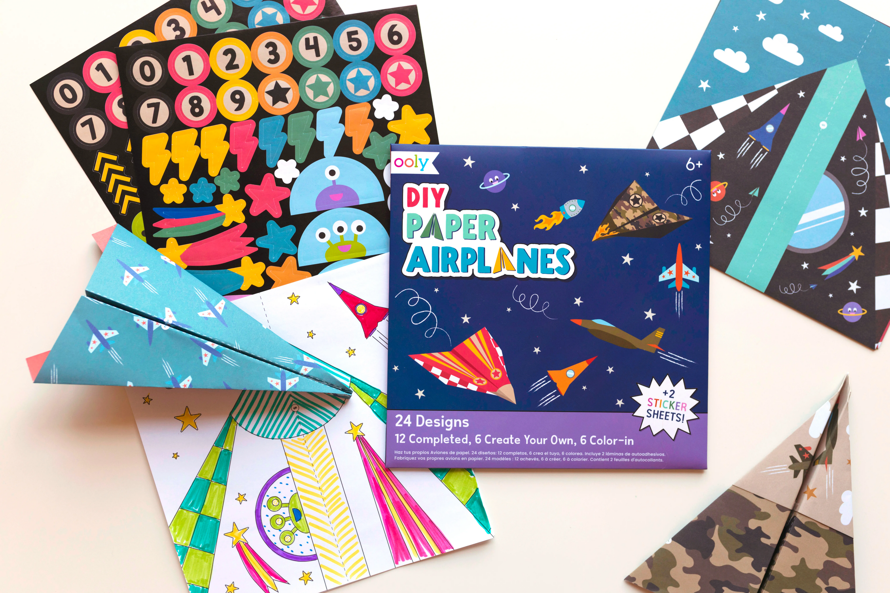 Collection of contents of OOLY DIY Paper Airplanes Activity Kit with stickers and coloring pages