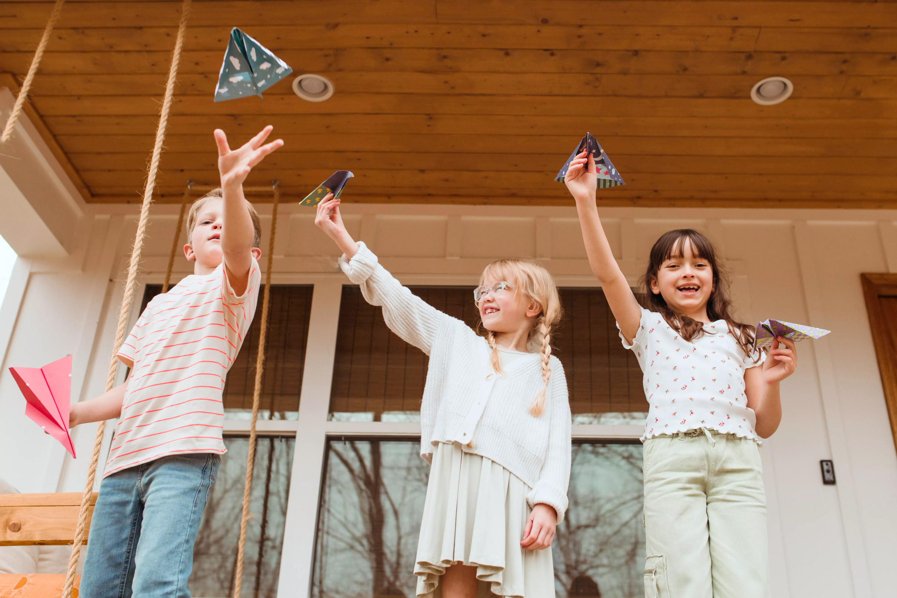Three kids launching paper airplanes made from OOLY DIY Paper Airplanes Activity Kit