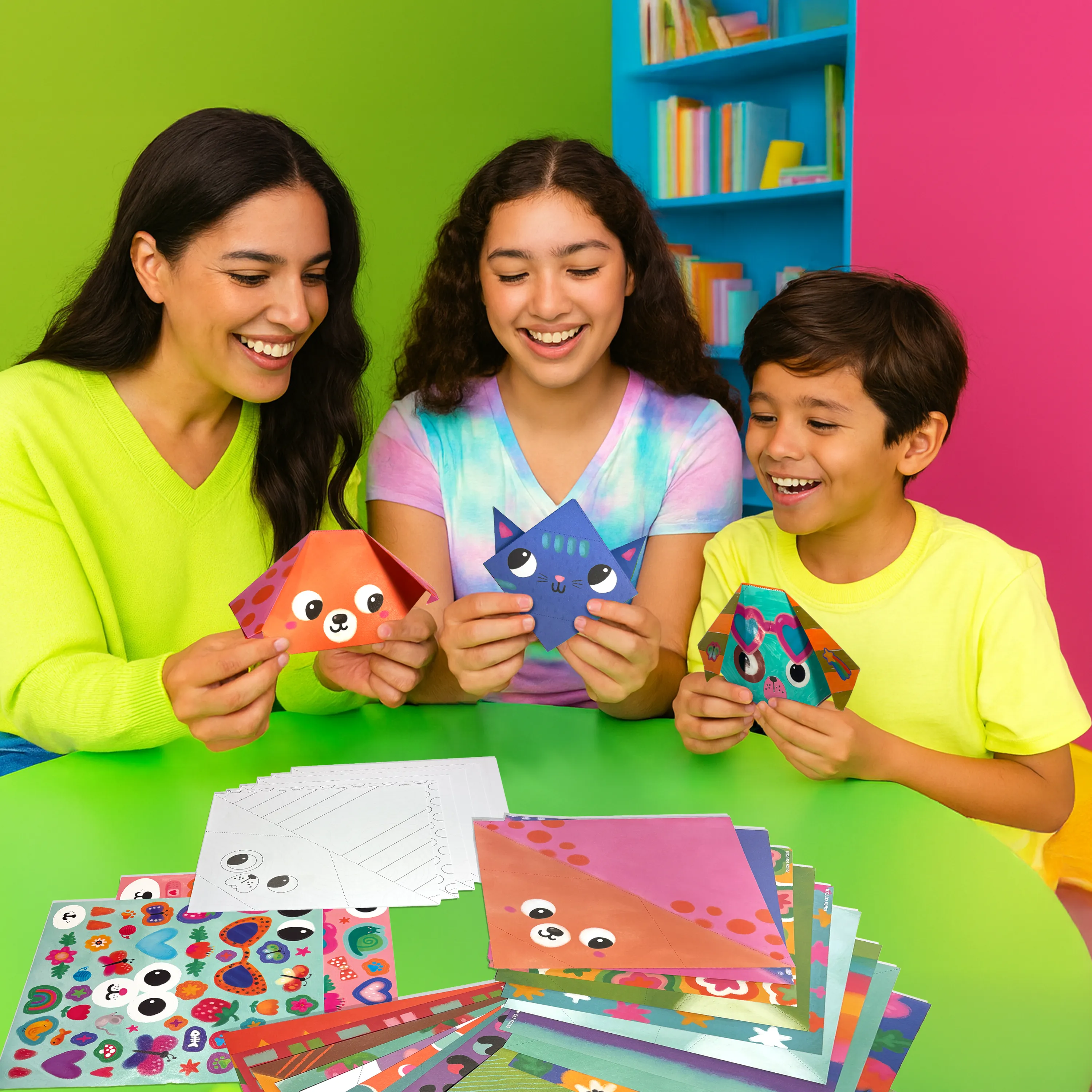 Family holding completed origami pets from the OOLY DIY Pet Pals Origami Activity Kit with a colorful background
