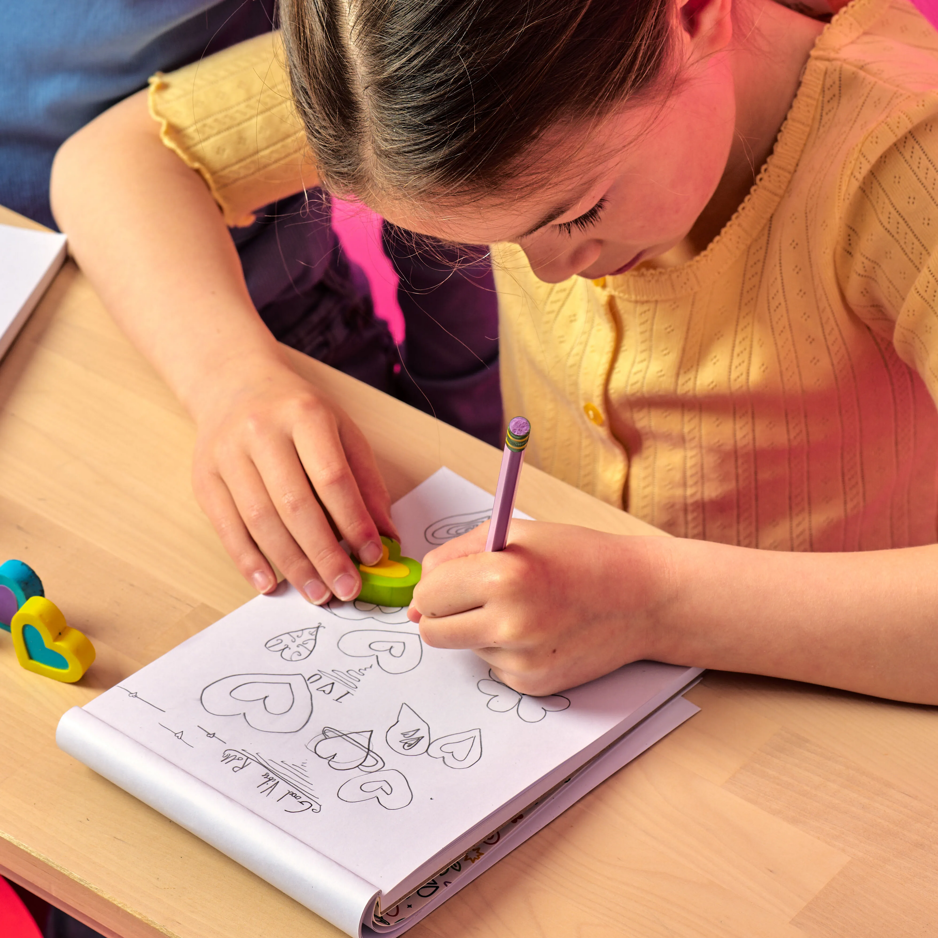 Girl drawing on a white sketchpad while holding an OOLY Hearts in Bloom Puzzle Eraser on wooden table
