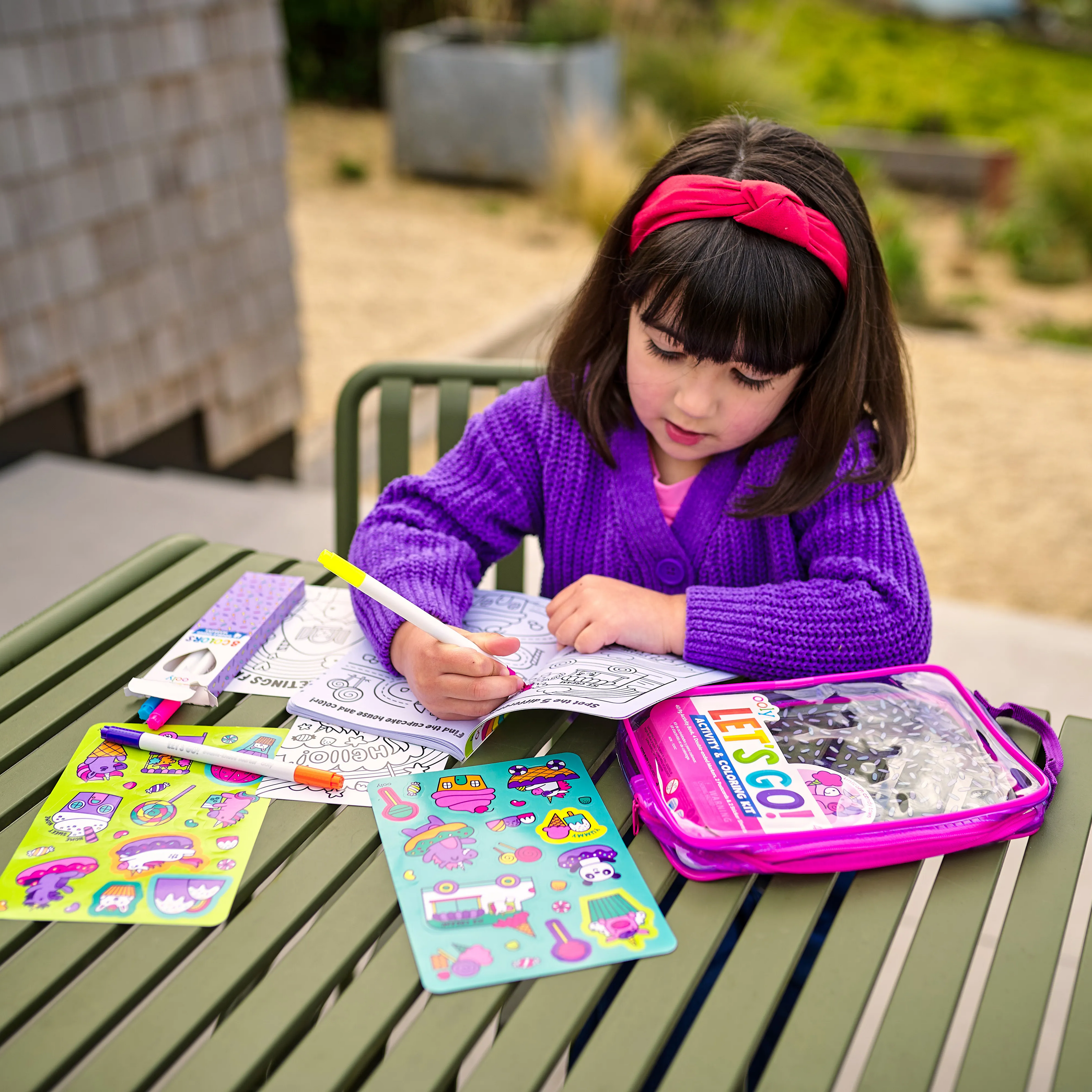 Girl coloring in Let’s Go! Activity & Coloring Kit on a park table