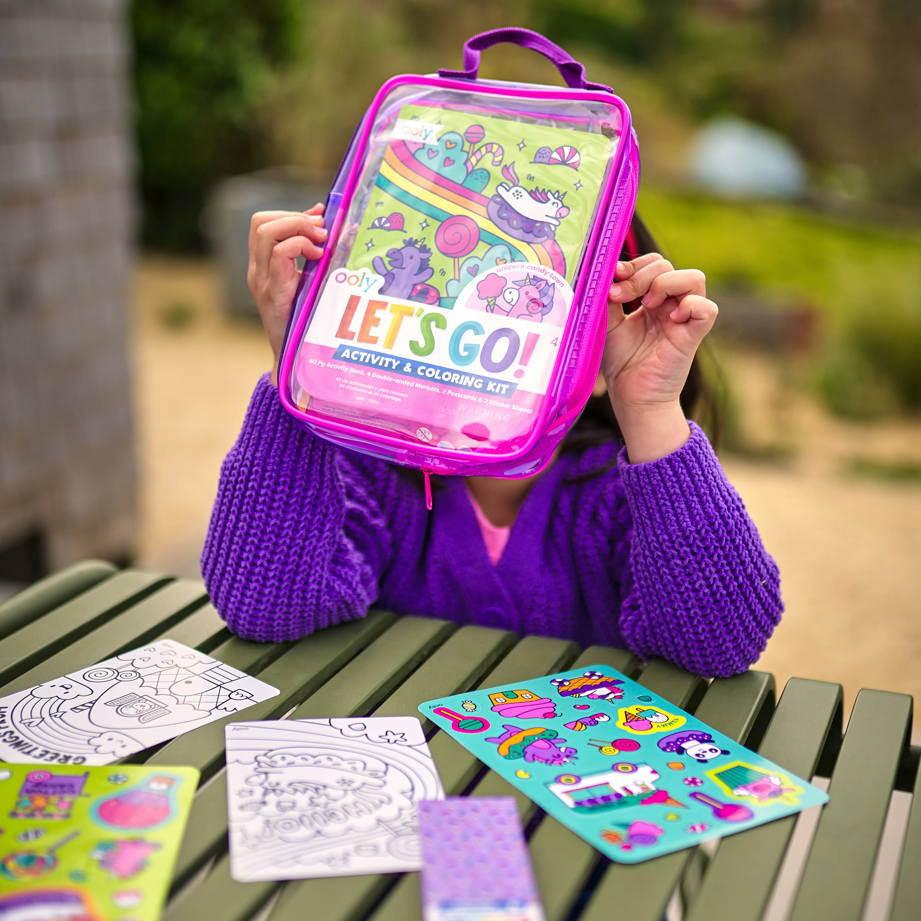 Girl holding Let’s Go! Activity & Coloring Kit on a park table