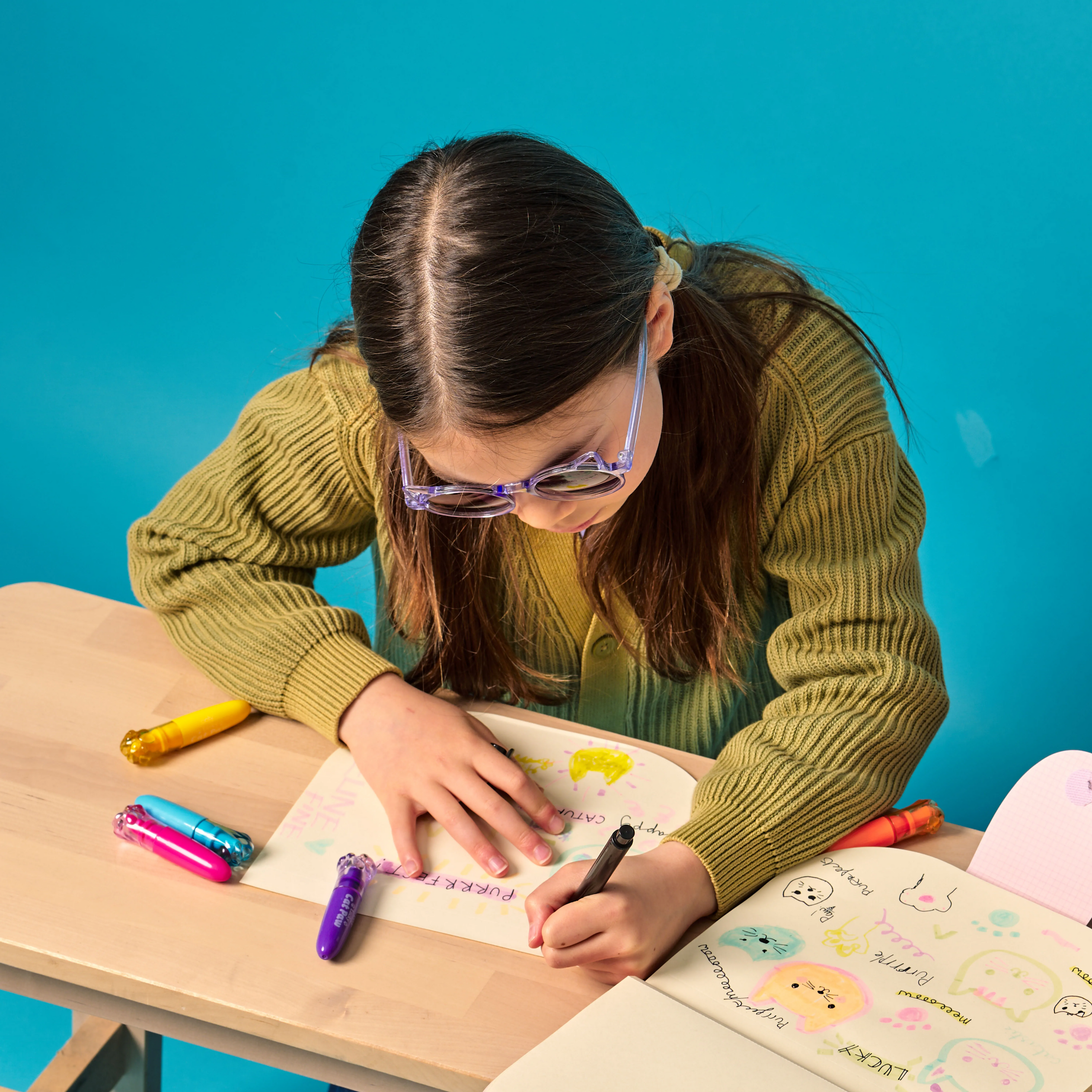 Girl with sunglasses highlighting cat drawings with OOLY Lucky Cat Paw Scented Neon Highlighters on a wooden table