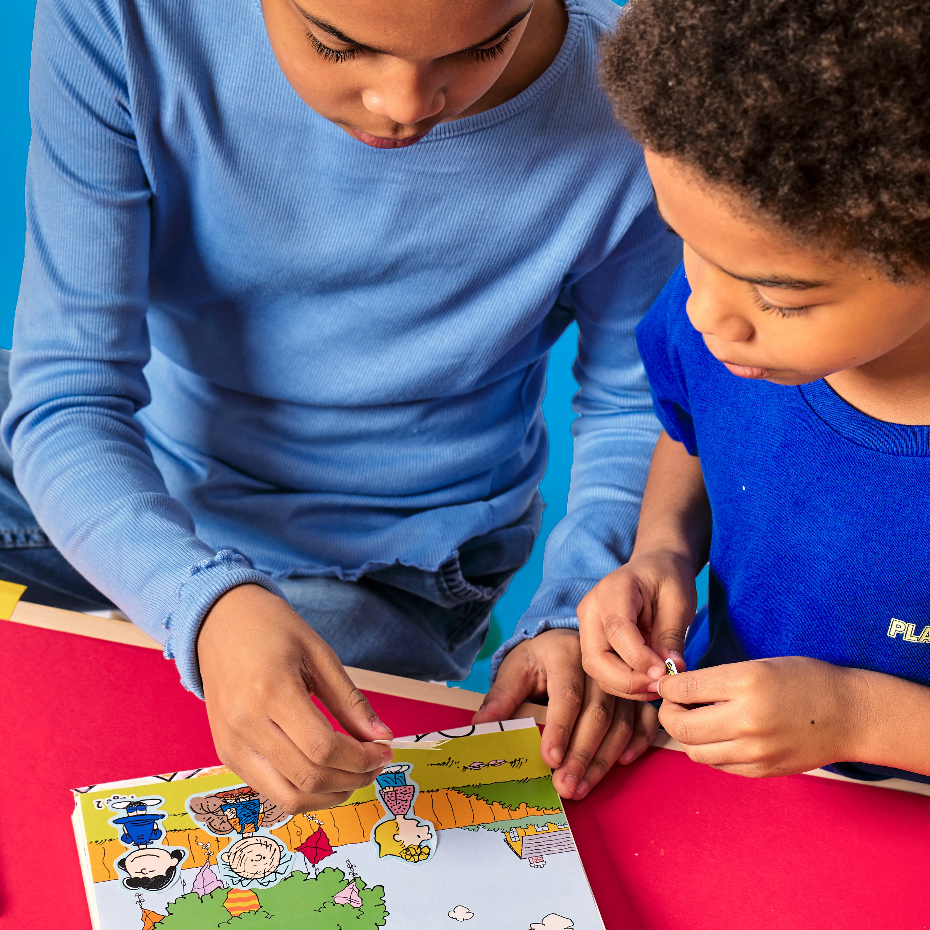 Two kids applying stickers to a OOLY x Peanuts Coloring Activity & Sticker Kit