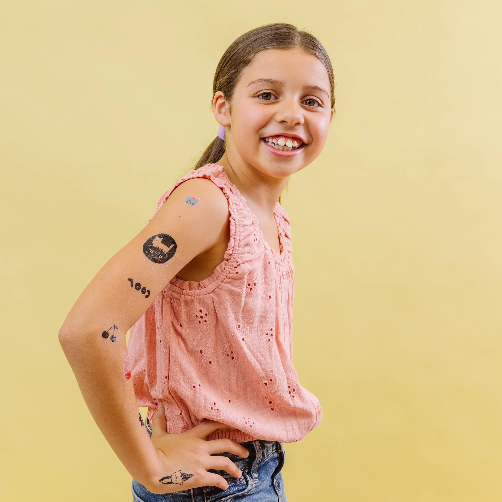 Girl with several Tattoo-Palooza x Suzy Ultman: Temporary Tattoos on yellow background