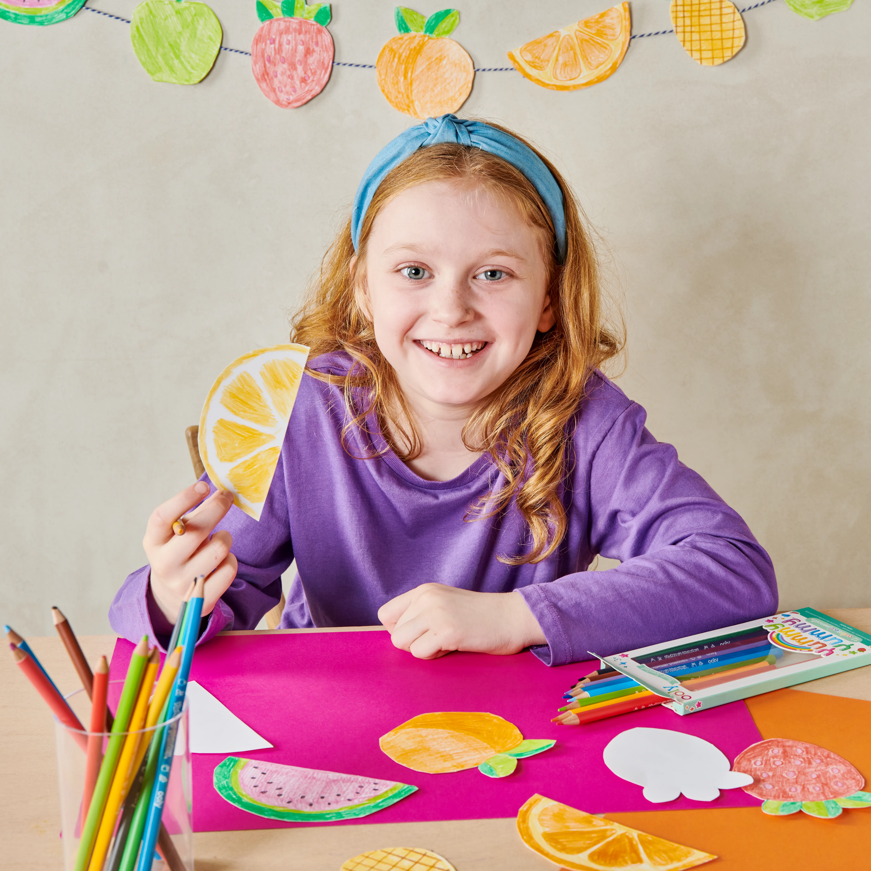 Girl at table smiling with OOLY Yummy Yummy Fruit Scented Colored Pencils
