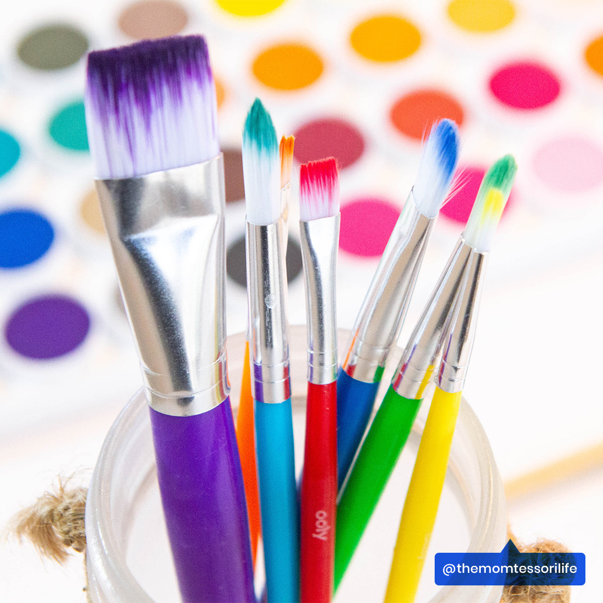 Close up of OOLY Lil Paint Brushes in a jar with watercolor paint pad in background