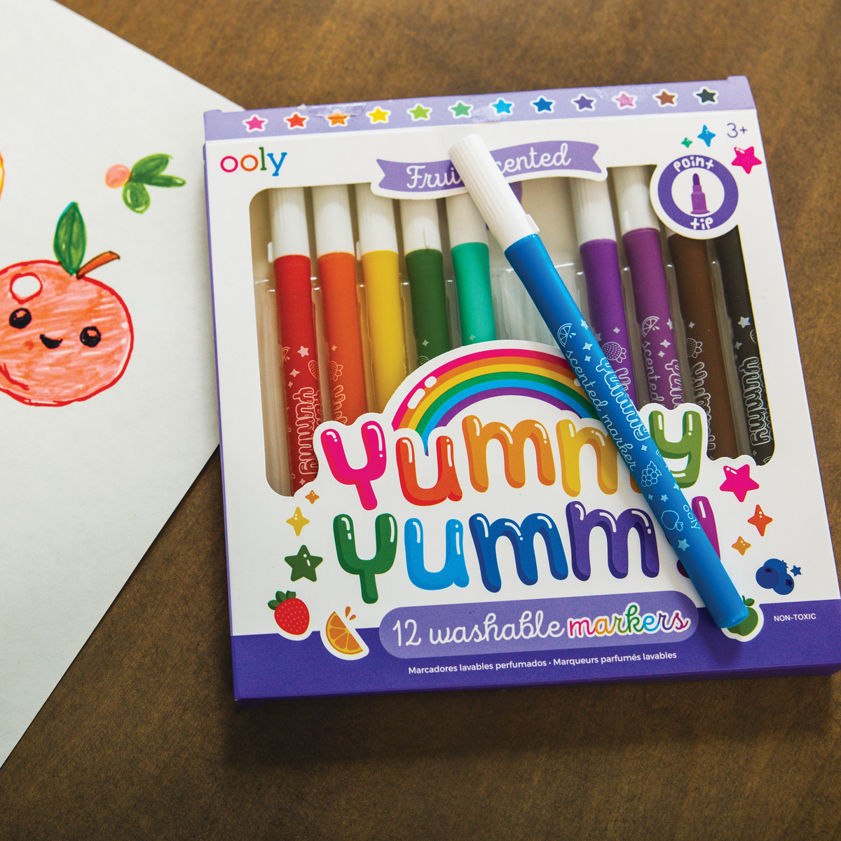 Set of Yummy Yummy scented markers on a wooden table next to cute fruit drawing